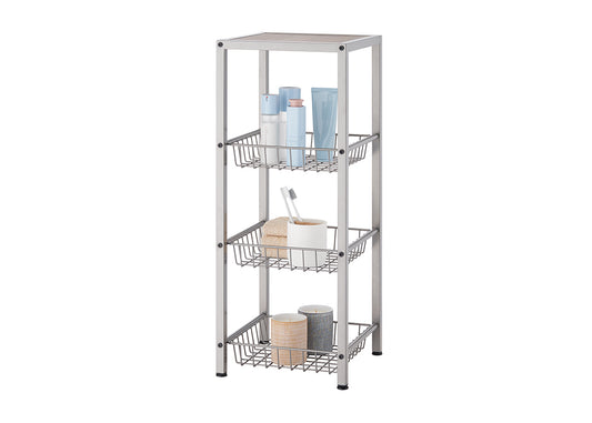 A champagne colored, four-tier metal shelving unit with three slatted baskets is shown against a white background. The shelves hold various bathroom items, including lotions, a toothbrush, towels, and decorative candles.