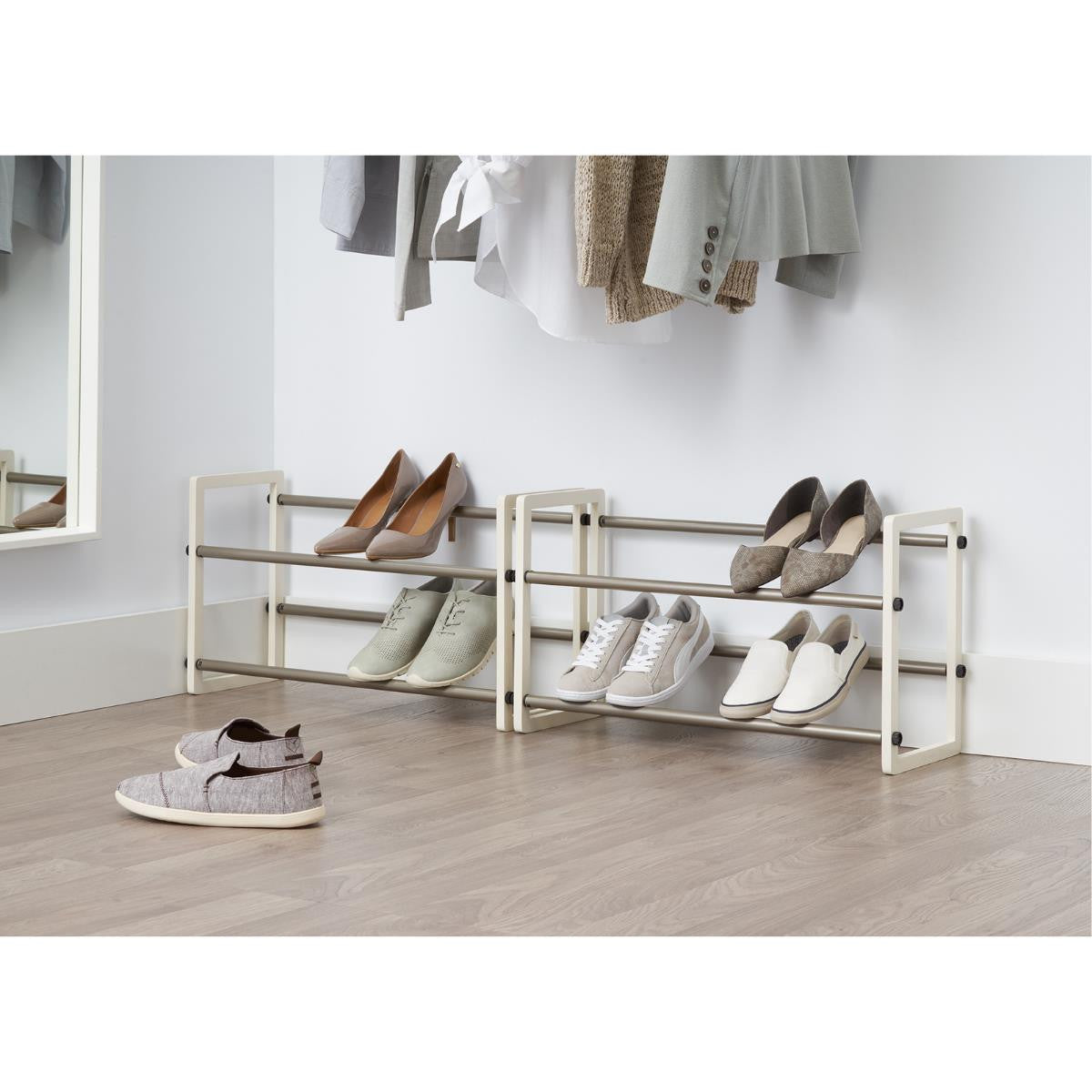 A two-tier expandable shoe rack with several pairs of shoes on it. The rack is placed in a closet, with clothes hanging above it.