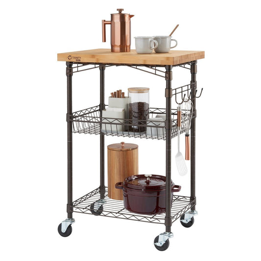 A three-tiered bronze metal kitchen cart with a light brown bamboo top is shown against a white background. The cart holds various kitchen items, including mugs, a French press, jars, and a pot.