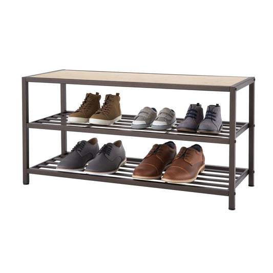 A three-tiered bronze anthracite metal shoe bench with a light brown wooden top displays various pairs of shoes. The bench has two lower grated shelves holding sneakers and dress shoes, while the top wooden surface is empty.
