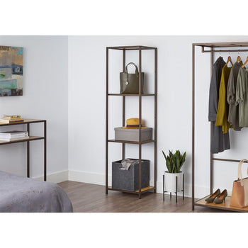 A tall, four-tiered metal shelf with bamboo surfaces stands against a white wall, holding a green purse, a gray box with a yellow hat, and a gray fabric bin. This shelving unit appears to be the Trinity 4-Tier Bamboo Shelving Tower, offering stylish and functional storage.