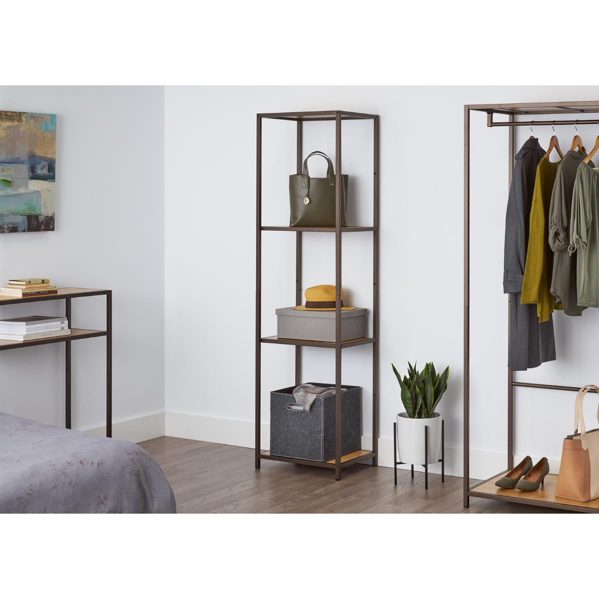 A tall, four-tiered metal shelf with bamboo surfaces stands against a white wall, holding a green purse, a gray box with a yellow hat, and a gray fabric bin. This shelving unit appears to be the Trinity 4-Tier Bamboo Shelving Tower, offering stylish and functional storage.