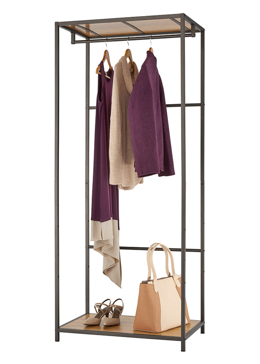 A bronze-colored metal garment rack stands against a white background, showcasing three hanging garments: a long purple dress, a light brown sweater, and a purple cardigan. Below, on a wooden shelf, are a pair of brown heeled sandals and a beige and brown tote bag.