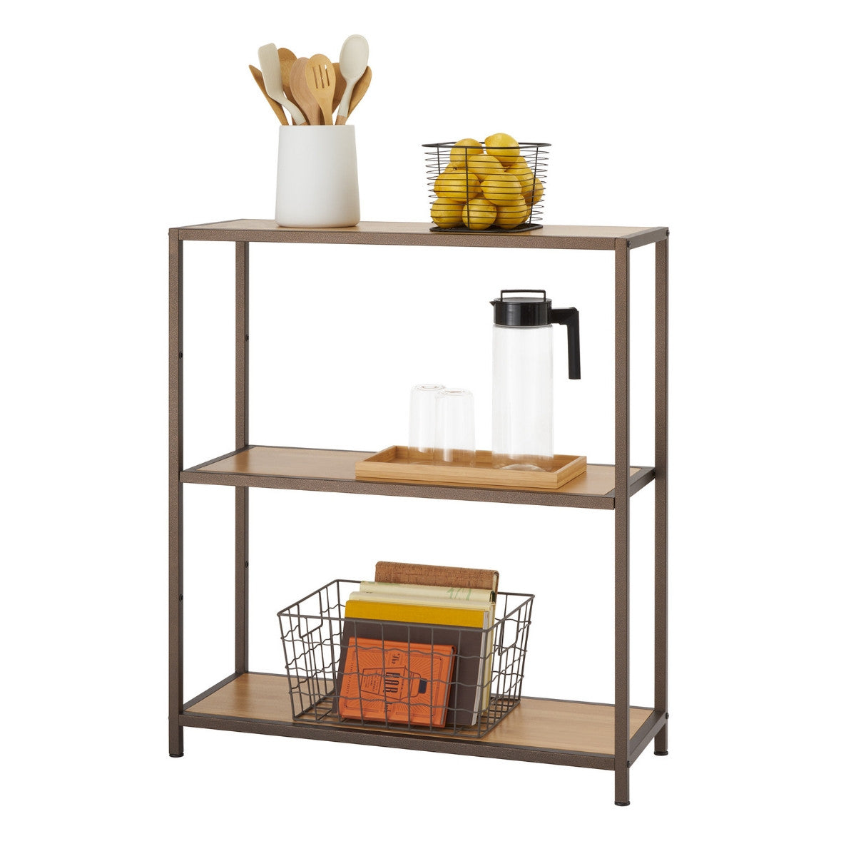 A three-tiered bronze anthracite shelving rack filled with kitchen items. The top shelf holds a white ceramic utensil holder with wooden kitchen tools and a black wire basket filled with yellow lemons. The middle shelf contains a wooden tray with a clear pitcher and two clear glasses. The bottom shelf holds a dark wire basket filled with books.