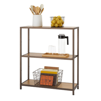 A three-tiered bronze anthracite shelving rack filled with kitchen items. The top shelf holds a white ceramic utensil holder with wooden kitchen tools and a black wire basket filled with yellow lemons. The middle shelf contains a wooden tray with a clear pitcher and two clear glasses. The bottom shelf holds a dark wire basket filled with books.