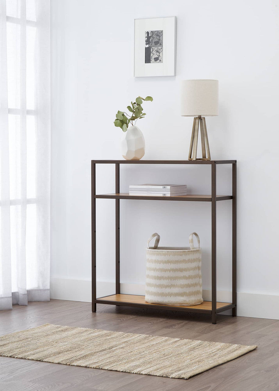 A bronze anthracite three-tiered rack used a a accent shelving unit in a living room. It has a lamp, a vase with greenery, and a striped basket adorn the table, complemented by a framed artwork on the wall.
