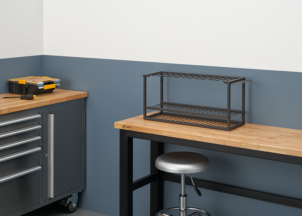 A workbench in a clean, organized garage or workshop. On the workbench sits a dark metal rack designed to hold tools, with an adjustable height stool tucked underneath.