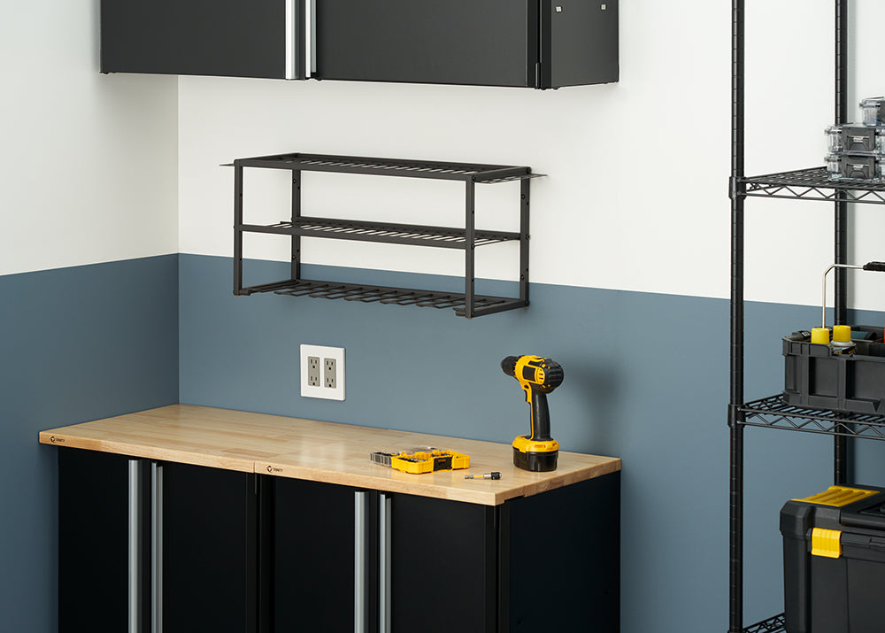 A black metal two-tier shelf with a built-in power tool rack is mounted on a two-toned wall. Below it, a black cabinet with a wooden workbench top holds a yellow and black power drill.
