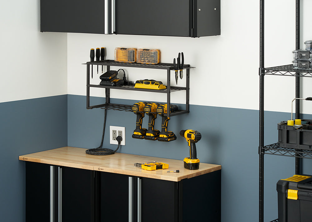 A metal-framed storage rack is mounted on a two-toned wall above a black cabinet with a wooden countertop. The rack holds several items, including a row of three DeWalt power drills, charging batteries, screwdriver bits, and various hand tools.