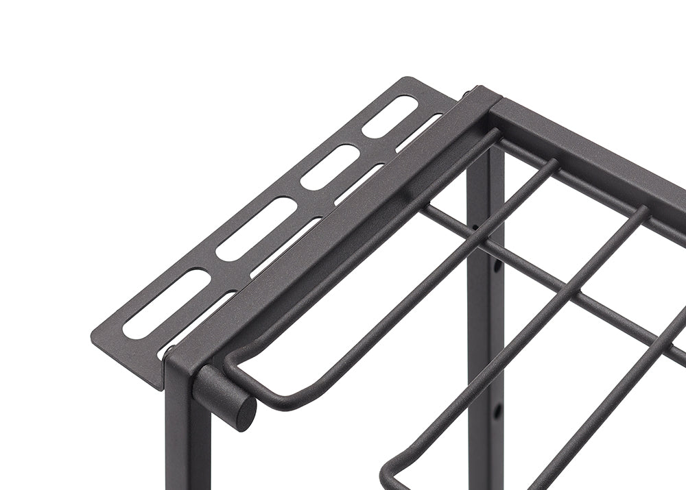 A close-up, eye-level shot shows the upper corner of a charcoal-gray metal wire rack. The rack features a perforated top shelf and a section below with thick parallel wires for storage.