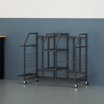 A black metal rolling storage cart stands on a garage floor against a blue and white wall. The multi-tiered organizer features various shelves and slots, next to a black cabinet with a wood countertop.
