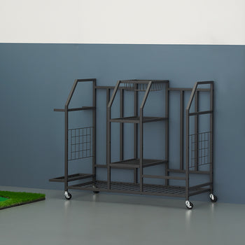 A black metal rolling storage rack with multiple tiered shelves and partitions stands on a garage floor against a blue-grey wall. The multi-purpose organizer is next to a indoor putting green with a ball and flag on the left, and a blue backpack hangs from a slat wall panel to the right.