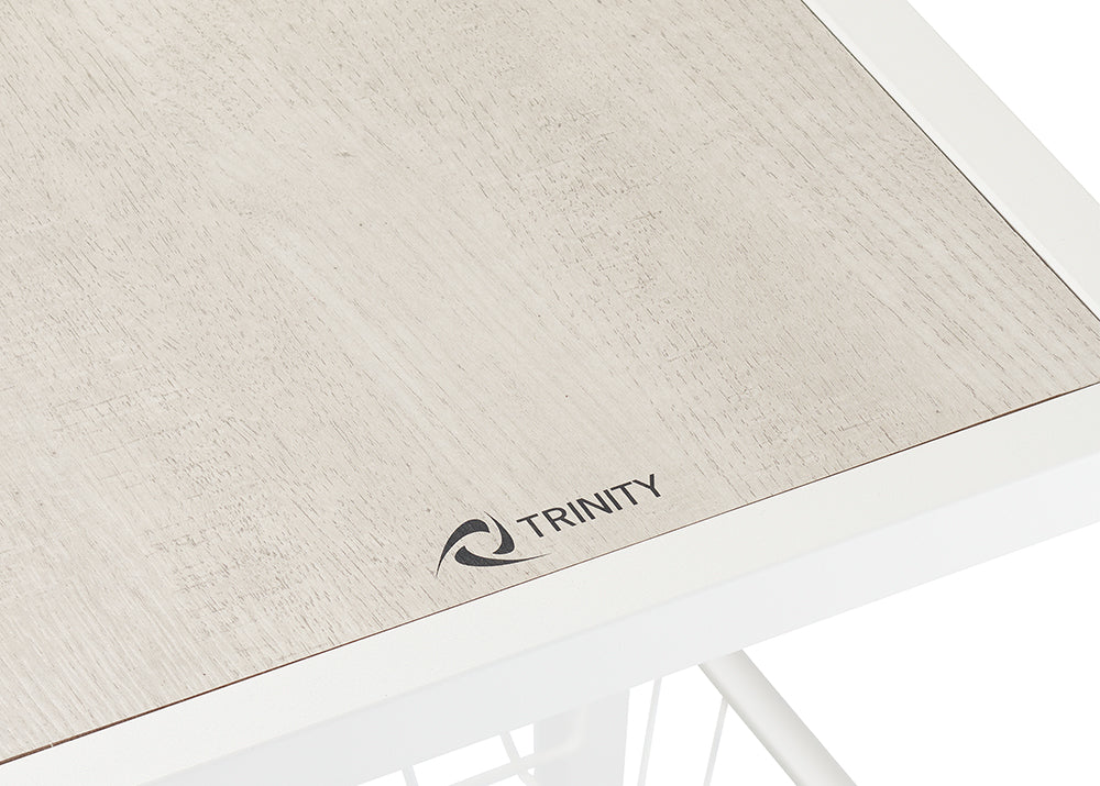 A close-up shot shows a light wood-grain surface with a dark grey "TRINITY" logo in the bottom right corner, featuring a stylized wave or swirl design next to the word. The surface is framed by a white border, indicating it's a shelf top.