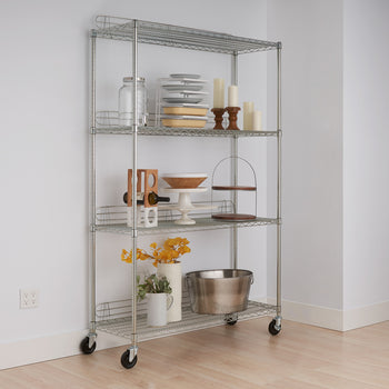 A four-tier chrome wire shelving unit with wheels stands against a white wall on a light wood floor. The shelves hold various kitchen and decorative items, including plates, jars, candles, a wine rack, and serving dishes.