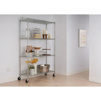 A four-tier chrome wire shelving unit with wheels stands against a white wall on a light wood floor. The shelves hold various kitchen and decorative items, including plates, jars, candles, a wine rack, and serving dishes.