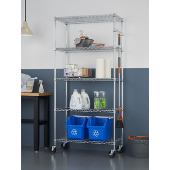 A tall, five-tiered chrome wire shelving unit on wheels holds various household and cleaning supplies in a garage. The shelves contain items such as cleaning sprays, laundry detergent, paper towels, blue recycling bins, and a mop and broom attached to the side.