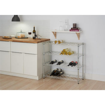 A chrome, 4-tier wire wine rack holds multiple bottles of wine in a kitchen setting. The rack stands on a light wood floor next to white kitchen cabinets, with a floating white shelf above it holding books and glassware.