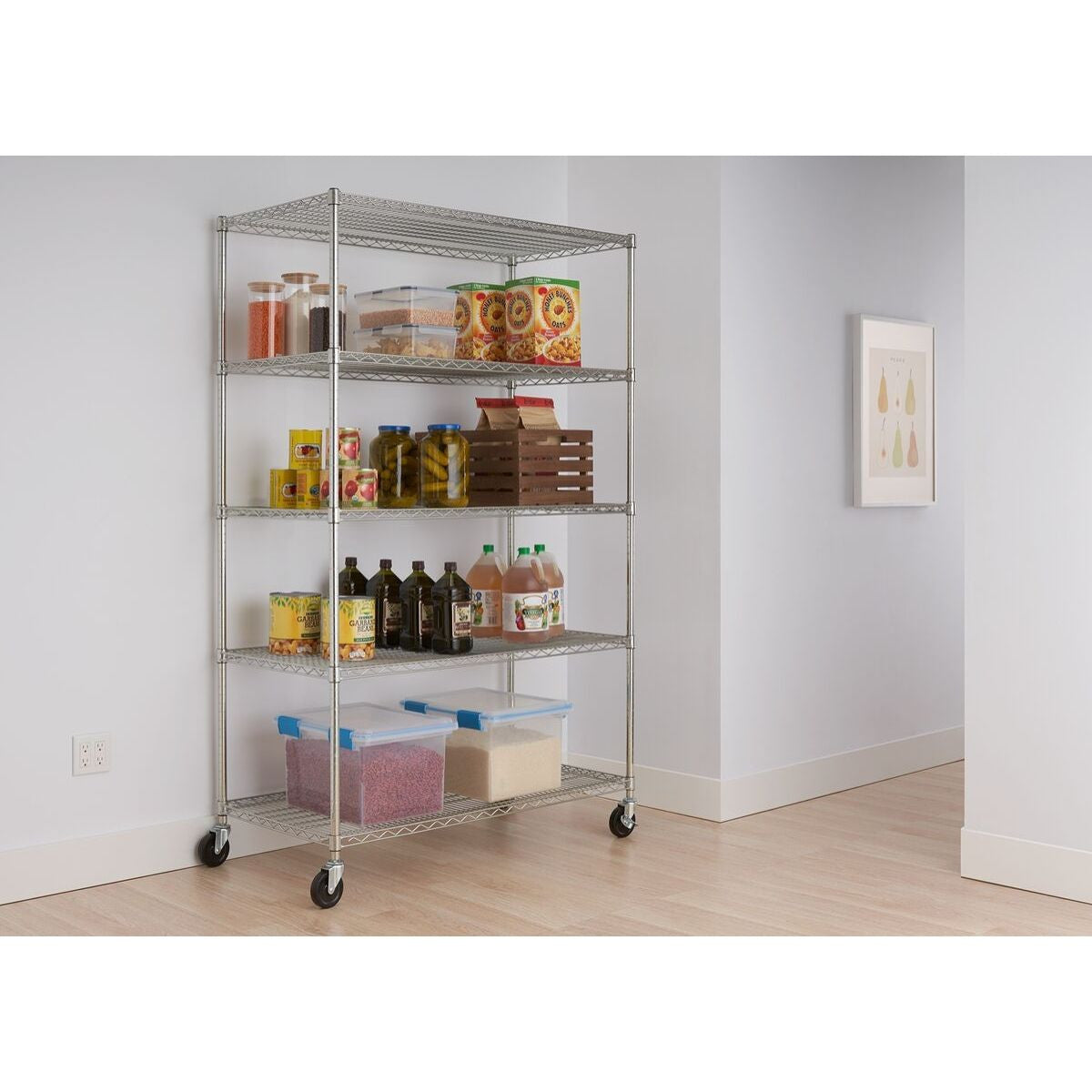 A tall, five-tier wire shelving rack on wheels is shown against a white wall in a room with a light wooden floor. The shelves hold various pantry items, including jars, boxes of cereal, canned goods, bottles, and clear plastic storage containers.