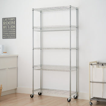 A 5-tier wire shelving rack with baskets and wheels stands against a white wall in a laundry room. A laundry basket sits on the floor to the left, and a rolling laundry sorter is on the right.