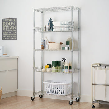 A silver wire shelving unit with five tiers stands in a laundry room, holding various cleaning supplies and baskets. The unit is on wheels and sits next to a white laundry hamper and a sign with 