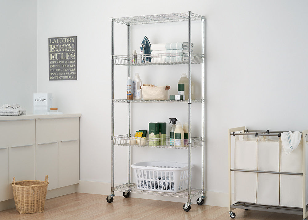 A silver wire shelving unit with five tiers stands in a laundry room, holding various cleaning supplies and baskets. The unit is on wheels and sits next to a white laundry hamper and a sign with "Laundry Room Rules."