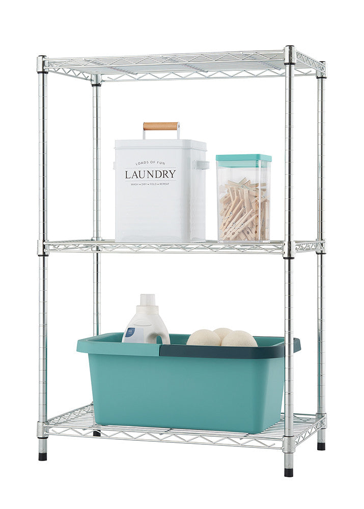 A silver wire shelving unit with three tiers is shown against a white background.  The shelves hold a white laundry bin, a clear container of clothespins, a bottle of detergent, and two round white objects.