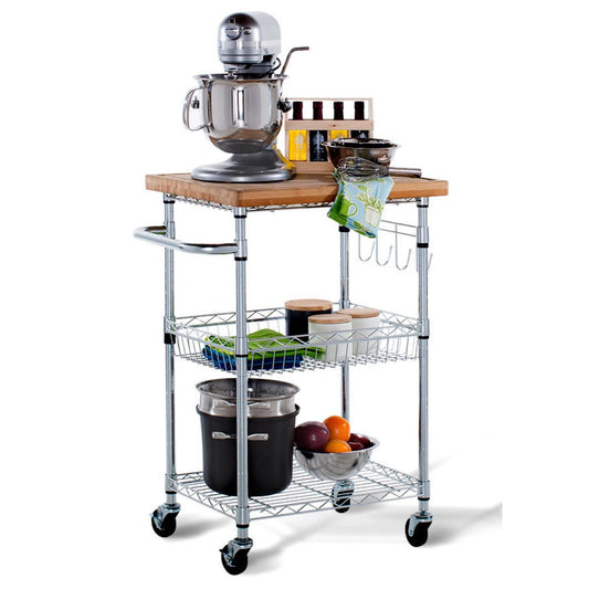 A three-tiered chrome kitchen cart with a light-colored bamboo wooden countertop is shown against a white background. The cart holds a stand mixer, bottles, bowls, jars, a pot, and a bowl of fruit.