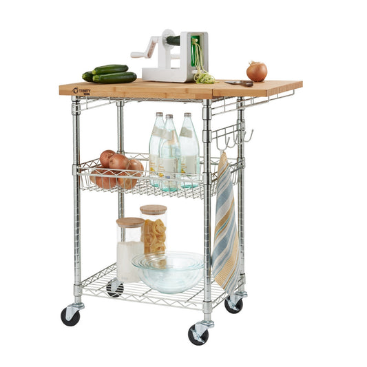 A chrome color kitchen cart with a light brown bamboo countertop one side of the wood top expanded with the hidden drop leaf metal kitchen cart it  holds vegetables, water bottles, and kitchen supplies. A white spiralizer sits on top of the countertop, creating zucchini noodles.