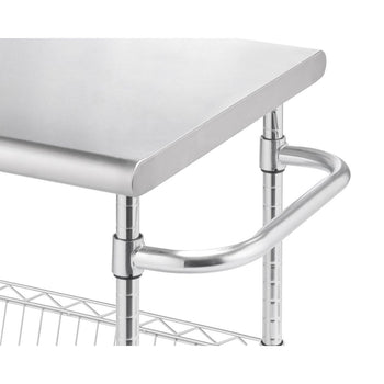 A close-up shows the corner of a stainless steel kitchen cart. The cart features a smooth, rounded-edge stainless steel top, tubular stainless steel legs, and a curved handle on one side, with a wire shelf visible underneath.