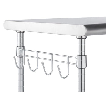 A close-up shows a section of a stainless steel service table. Visible are a portion of the top surface, two of the chrome-finished support poles, and a chrome wire rack with four hanging hooks attached to one of the poles.