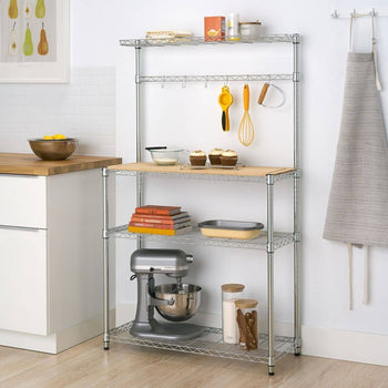A chrome metal baker's rack stands against a white tiled wall, holding various kitchen items. The rack features wire shelves, a light wood countertop, and hanging hooks with utensils.