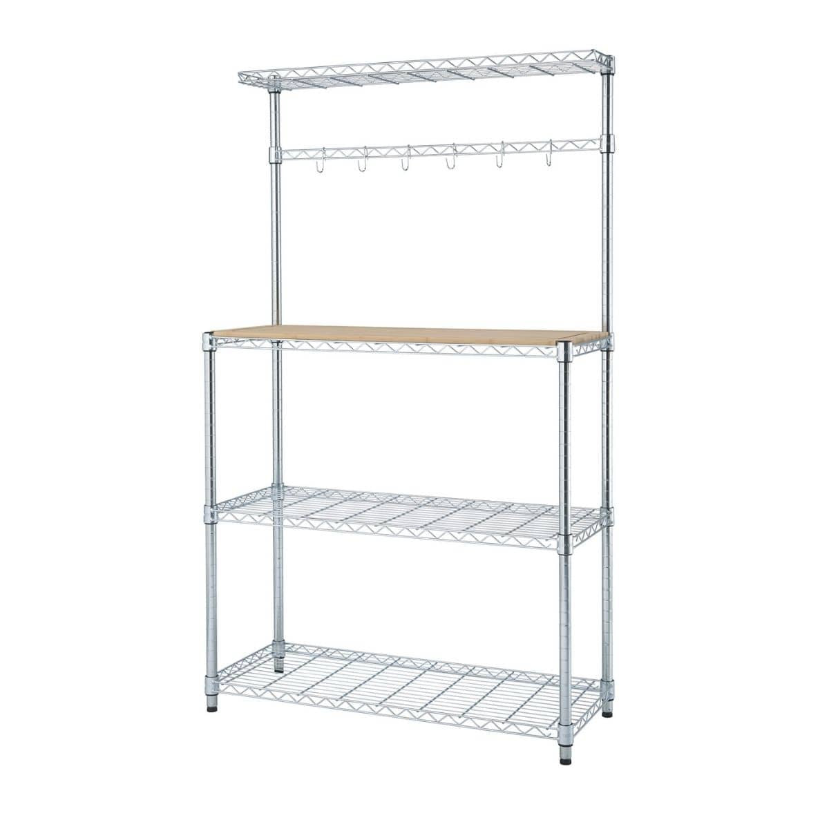 A chrome bakers rack with three wire shelves, a light brown wooden countertop, and an upper section with a wire shelf and hanging hooks is shown against a white background. The rack appears to be the Trinity Traditional Ecostorage Chrome Steel Bamboo Bakers Rack.