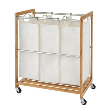 
A natural bamboo frame laundry cart with three removable white canvas bags is shown from a slightly elevated angle. The cart has chrome metal bars to hold the bags and four caster wheels for mobility.