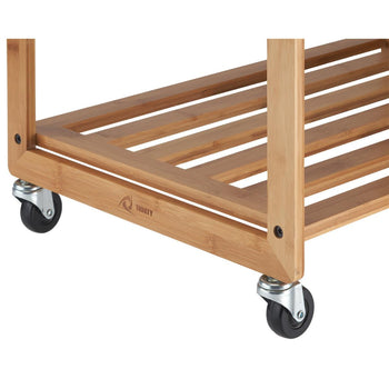 Base of a Trinity bamboo laundry cart, highlighting its natural wood construction and slatted lower shelf with Trinity logo embedded. Four silver-toned casters with black wheels are visible, two on each side, attached to the bamboo frame.