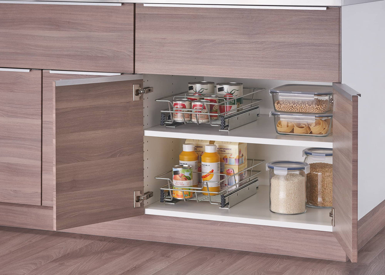 A partially open cabinet reveals two chrome wire sliding drawers installed on white shelves. The drawers contain various pantry items, including canned goods, bottles, and a bag of pasta, illustrating an organized storage solution.