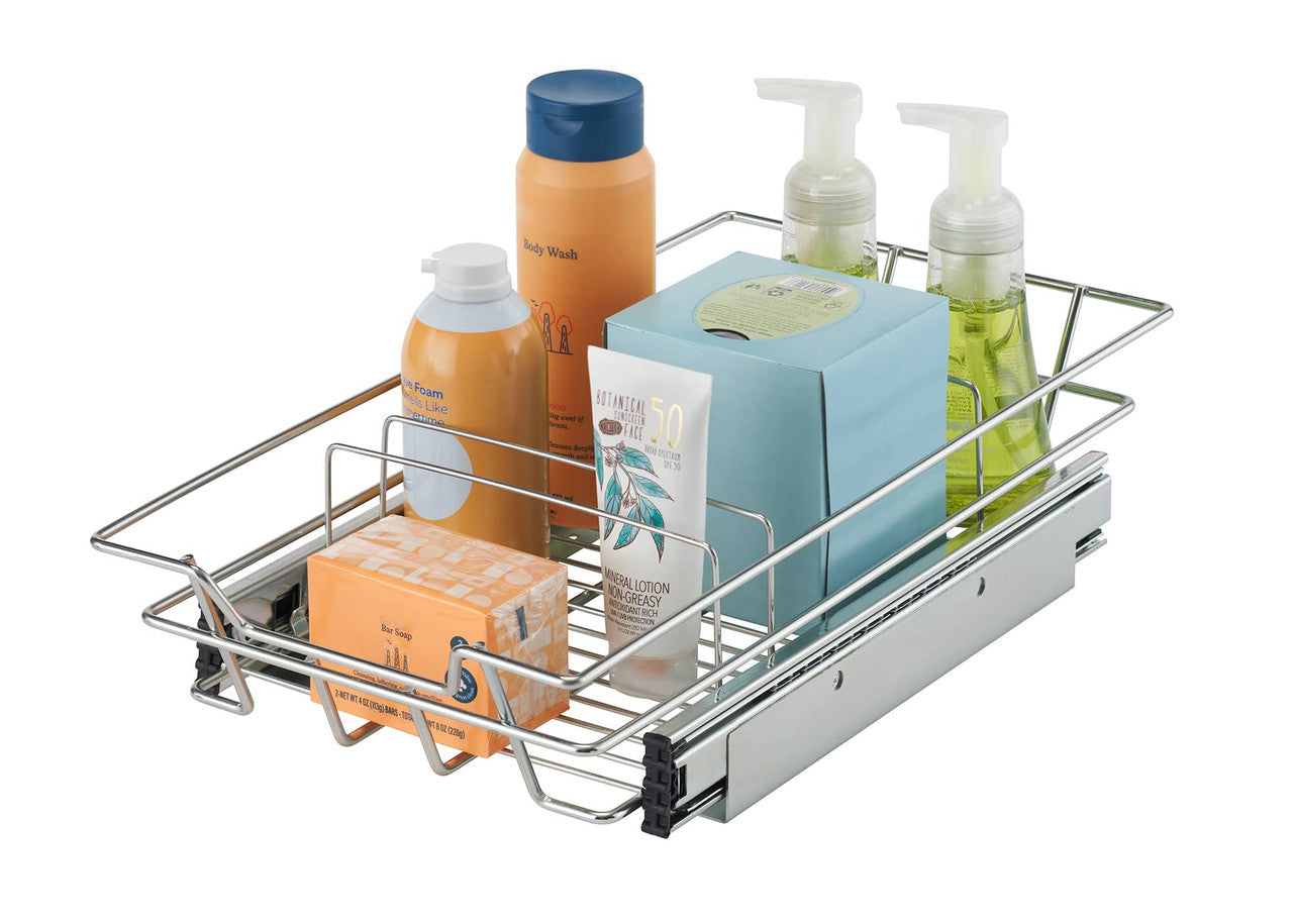 A chrome wire sliding drawer is shown extended, filled with various bathroom toiletries. The drawer contains a bar of soap in an orange box, a tube of lotion, a blue box of tissues, a bottle of orange foam soap, a tall orange bottle of body wash with a blue cap, and two clear pump bottles of green liquid soap.
