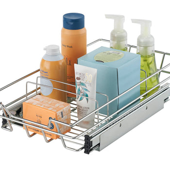 A chrome wire sliding drawer is shown extended, filled with various bathroom toiletries. The drawer contains a bar of soap in an orange box, a tube of lotion, a blue box of tissues, a bottle of orange foam soap, a tall orange bottle of body wash with a blue cap, and two clear pump bottles of green liquid soap.