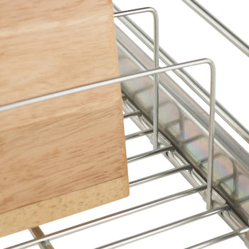A close-up shows a portion of a silver, sliding wire drawer. A light brown wooden cutting board rests inside the drawer, leaning against the wireframe.