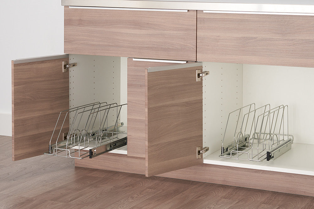 Two kitchen cabinets with light wood doors are partially open, revealing sliding metal organizers inside. The organizers have vertical dividers designed to hold bakeware or lids upright for easy access and storage.