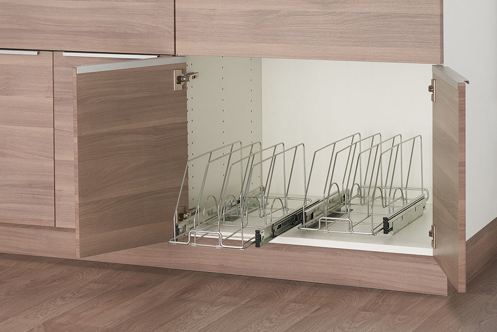 A partially open light brown cabinet reveals a white interior with two sliding wire racks designed to hold bakeware. Each rack features vertical wire dividers to keep items separated and organized.