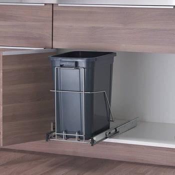 A dark gray rectangular trash can sits inside a light-colored kitchen cabinet. The trash can is mounted on a chrome sliding track, allowing it to be pulled out.