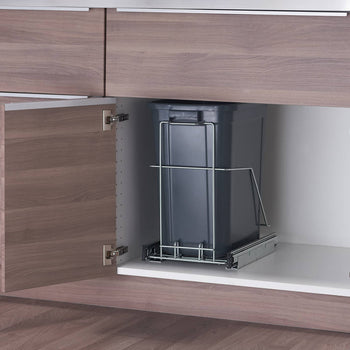 A gray rectangular trash can with a hinged lid sits inside a kitchen cabinet on a sliding metal frame. The cabinet doors are partially open, revealing the white interior and the mounted trash can.