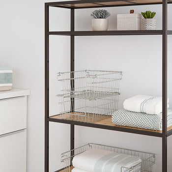 A close-up shot of a dark metal shelving unit with light wood shelves, holding wire baskets, folded towels, and small potted plants. The image focuses on the storage solutions within the shelving unit, showcasing its functionality and organization.
