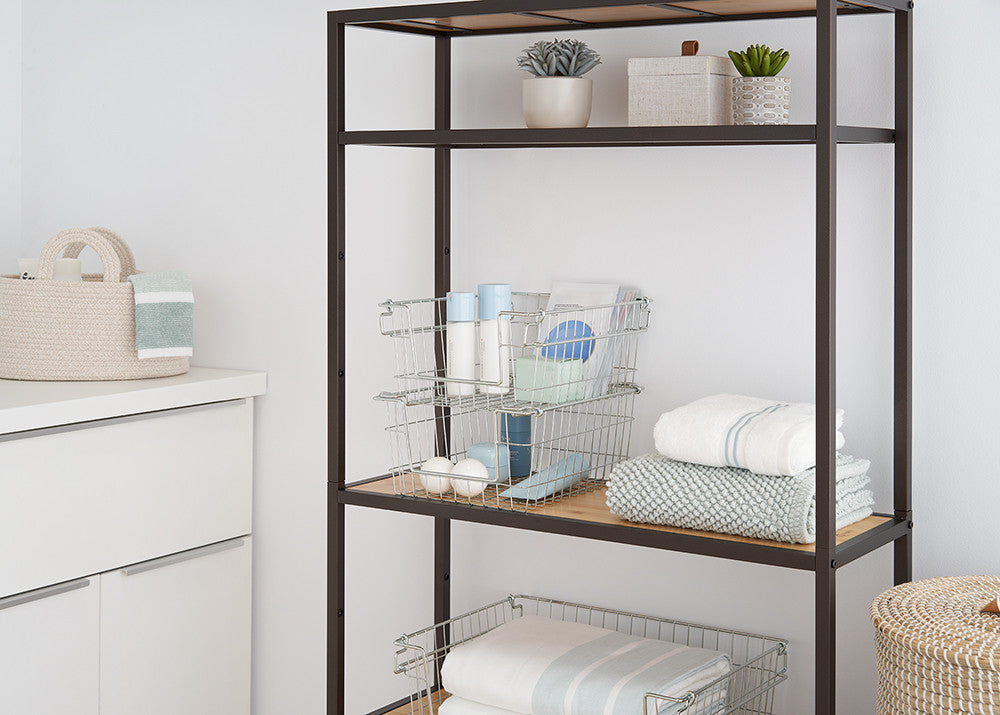 A close-up shot of a dark metal shelving unit with light wood shelves, holding wire baskets, folded towels, and small potted plants. The image focuses on the storage solutions within the shelving unit, showcasing its functionality and organization.