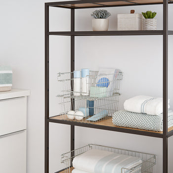 A close-up shot of a dark metal shelving unit with light wood shelves, holding wire baskets, folded towels, and small potted plants. The image focuses on the storage solutions within the shelving unit, showcasing its functionality and organization.