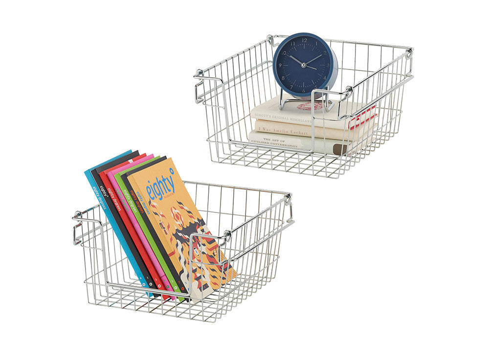 Two chrome wire baskets are shown on a white background. One basket contains a stack of books and a blue clock, while the other holds a stack of colorful books. The baskets are stackable and appear to be part of a storage solution.