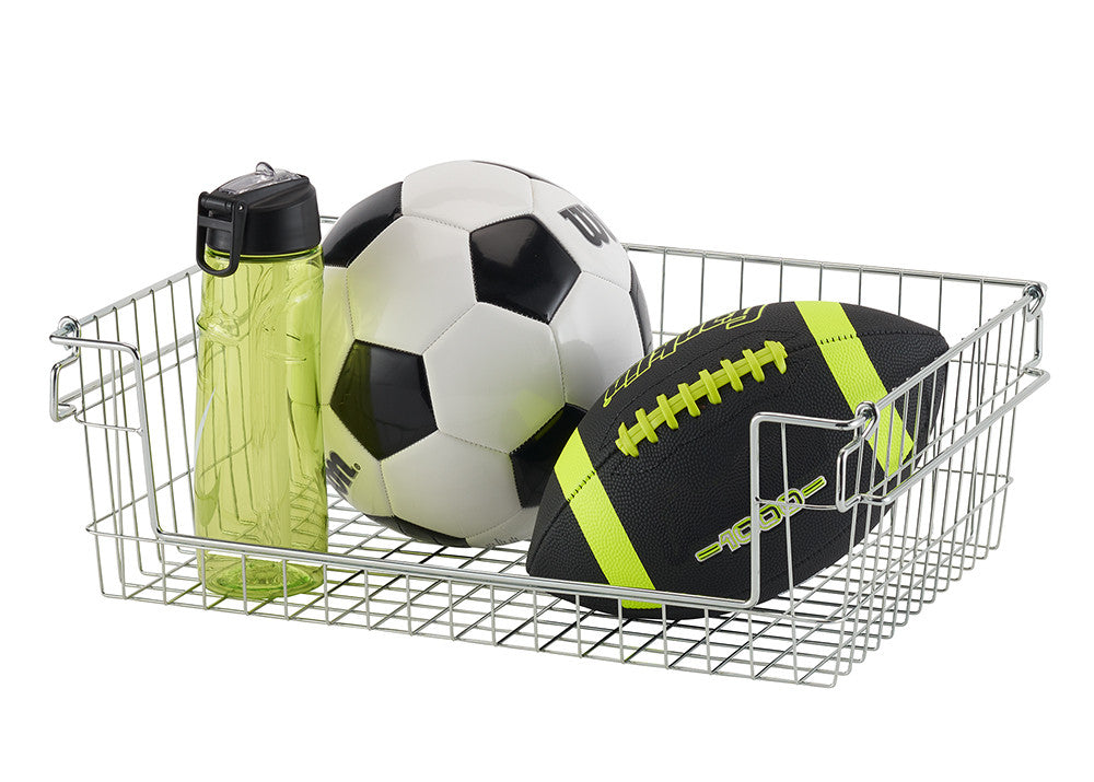 A chrome wire basket contains a green water bottle, a soccer ball, and a football. The basket is rectangular with a grid pattern and has handles on the sides.