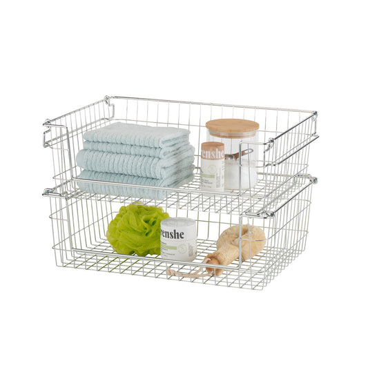 A studio shot of two chrome wire storage baskets stacked on top of each other, filled with various bathroom items. The baskets feature a grid pattern and are shown against a white background.