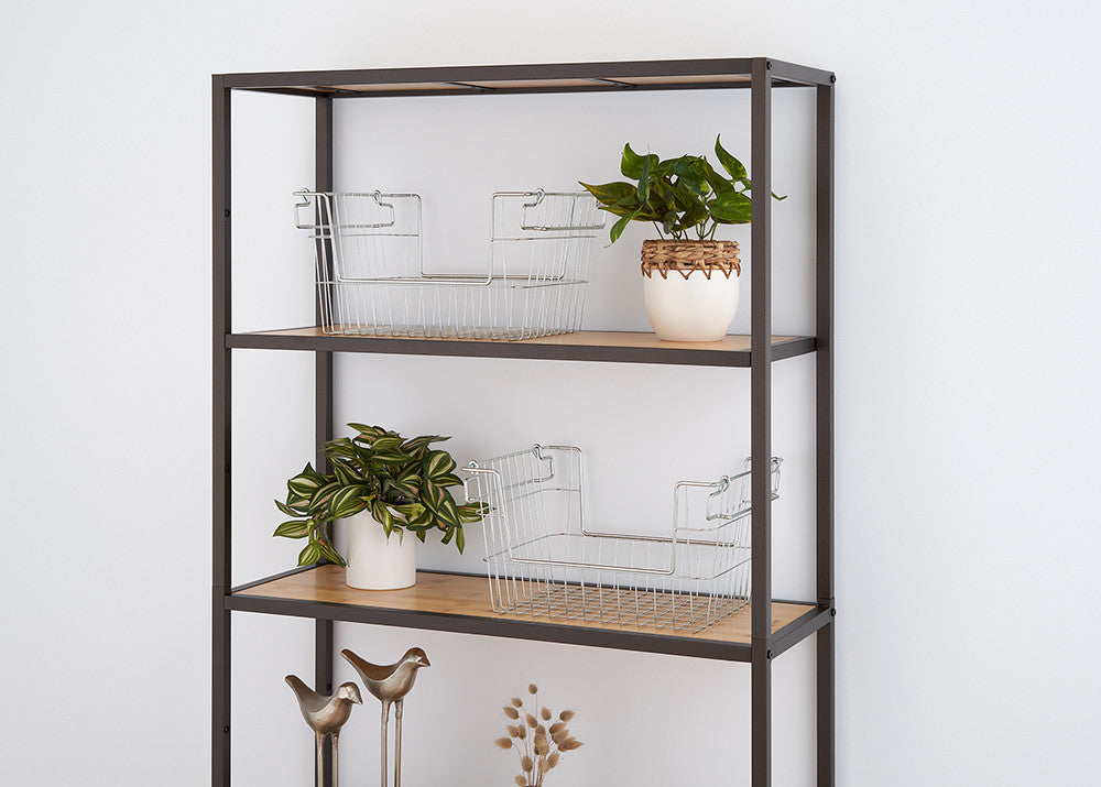 A modern, minimalist shelving unit with a black metal frame and wooden shelves is positioned against a white wall. The shelves hold wire storage baskets, small potted plants, and decorative metal bird figurines.