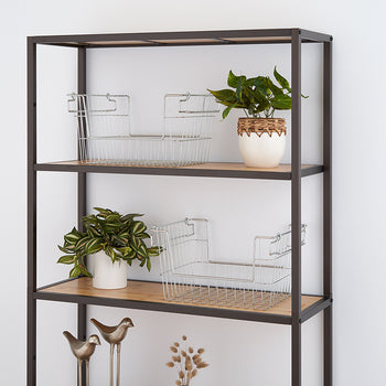 A modern, minimalist shelving unit with a black metal frame and wooden shelves is positioned against a white wall. The shelves hold wire storage baskets, small potted plants, and decorative metal bird figurines.